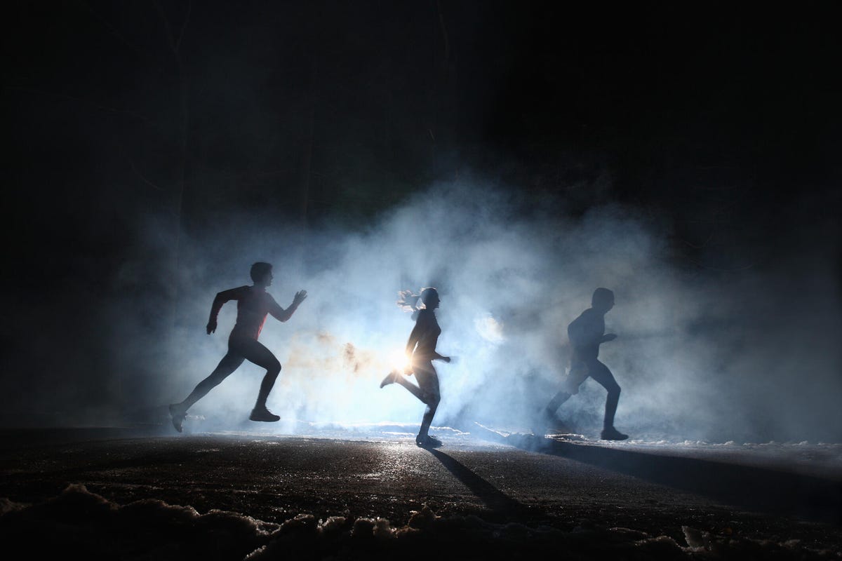 Three people running in the dark, surrounded by illuminated fog