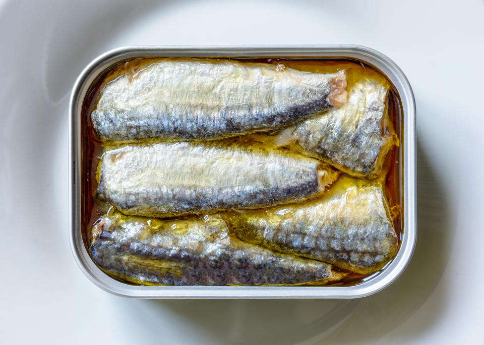 An open can of sardines in oil on a white plate seen from above.