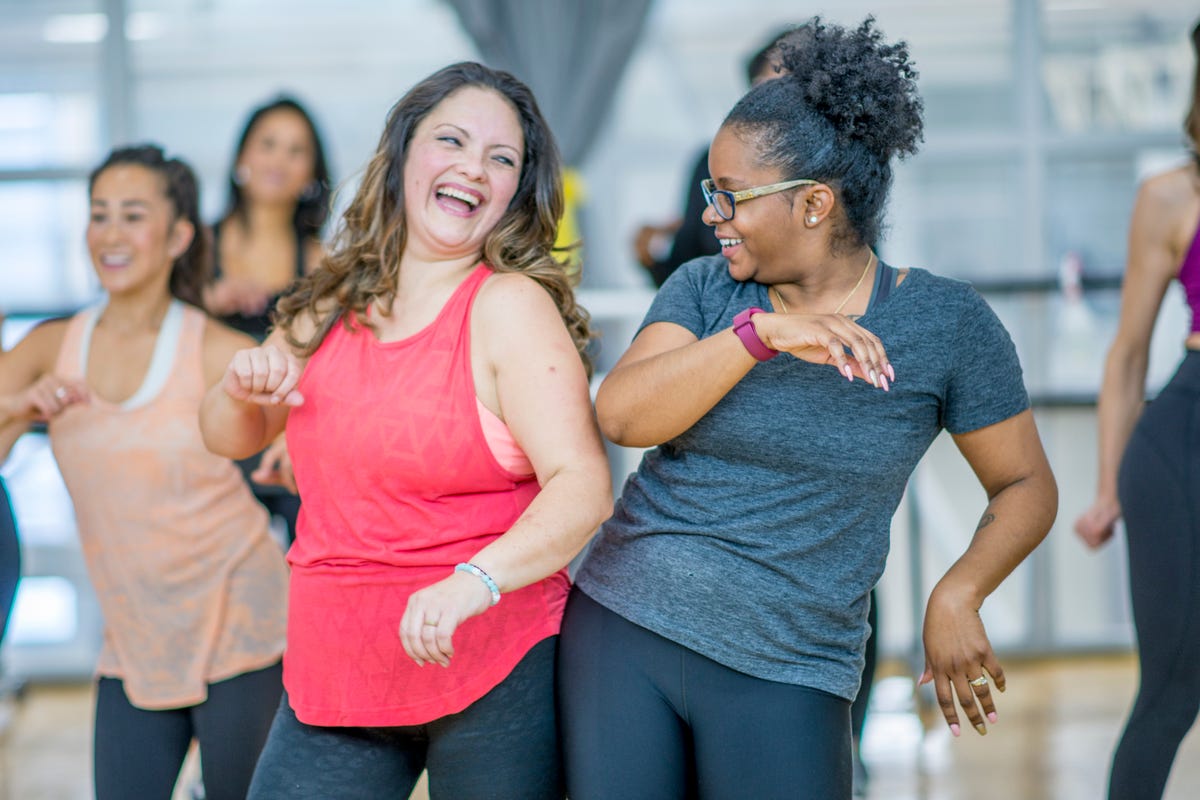 Two women in workout clothes dancing side by side and smiling